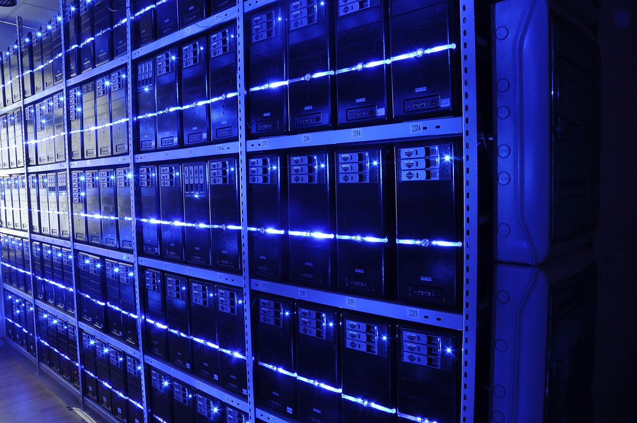An aisle of server racks in a data center, blue and white lights receding into the distance