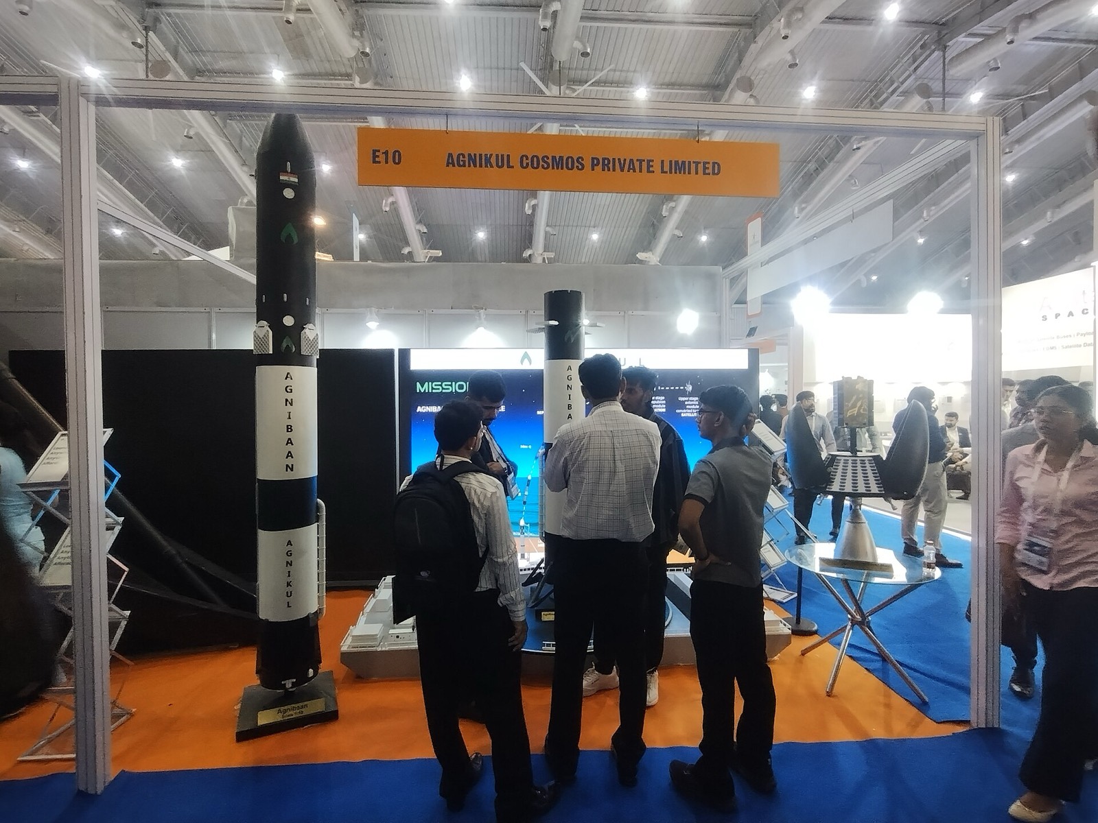 Agnikul Cosmos stall at an exhibition with two black and white Agnibaan rocket models and visitors.