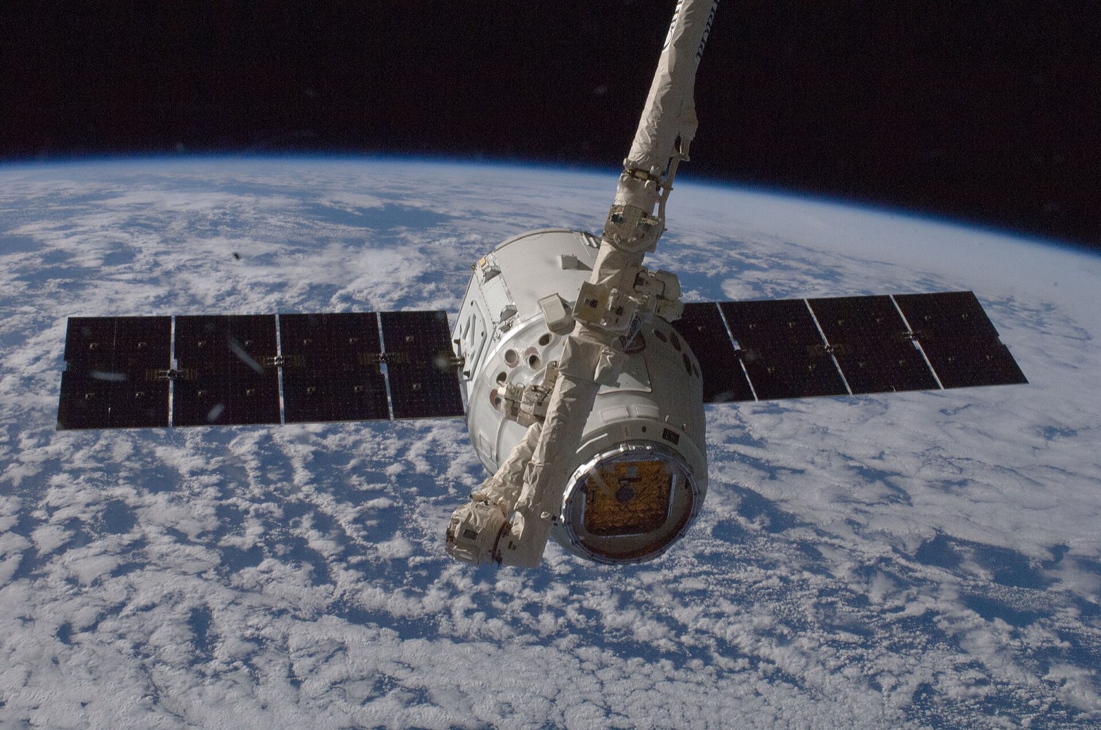 SpaceX’s first contracted Dragon cargo capsule held by the space station’s robotic arm above Earth