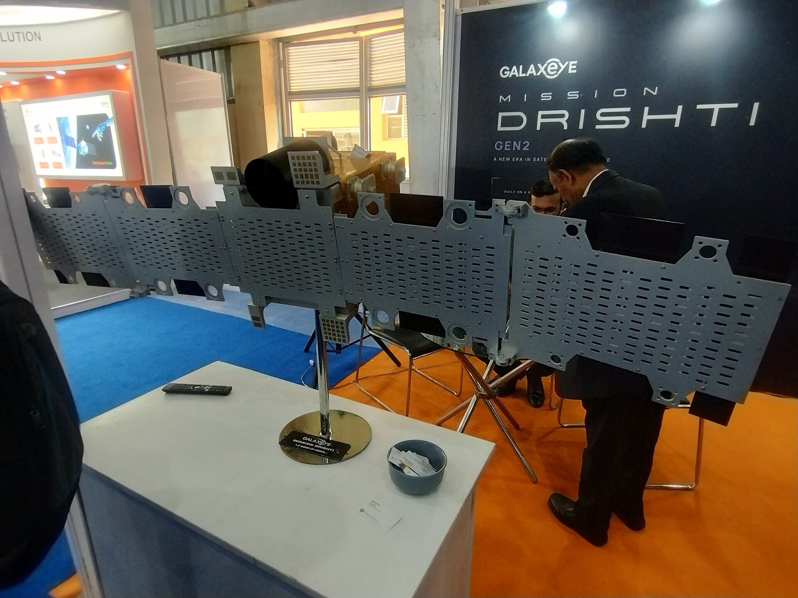 A model of GalaxEye’s Drishti satellite with long perforated grey panels on a stand, beside a Mission Drishti sign.