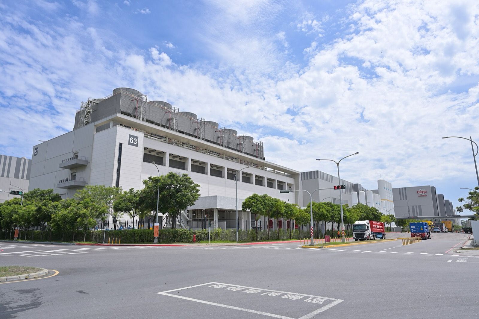 A large white TSMC fab building in Tainan under a blue sky, with trees and an empty road in front.