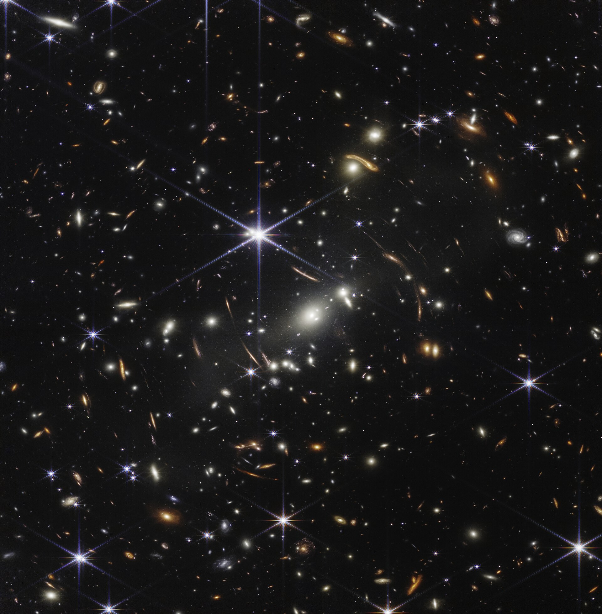 The James Webb Space Telescope's first deep field: thousands of galaxies, including faint arcs of light bent by a galaxy cluster's gravity, against the black of deep space.