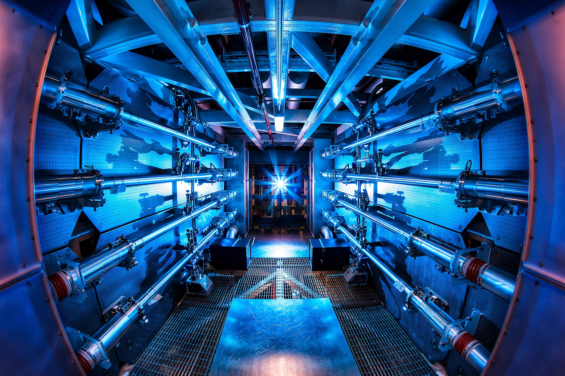 The interior of the National Ignition Facility, a vast cylindrical chamber of blue-lit laser preamplifier optics receding into the distance.