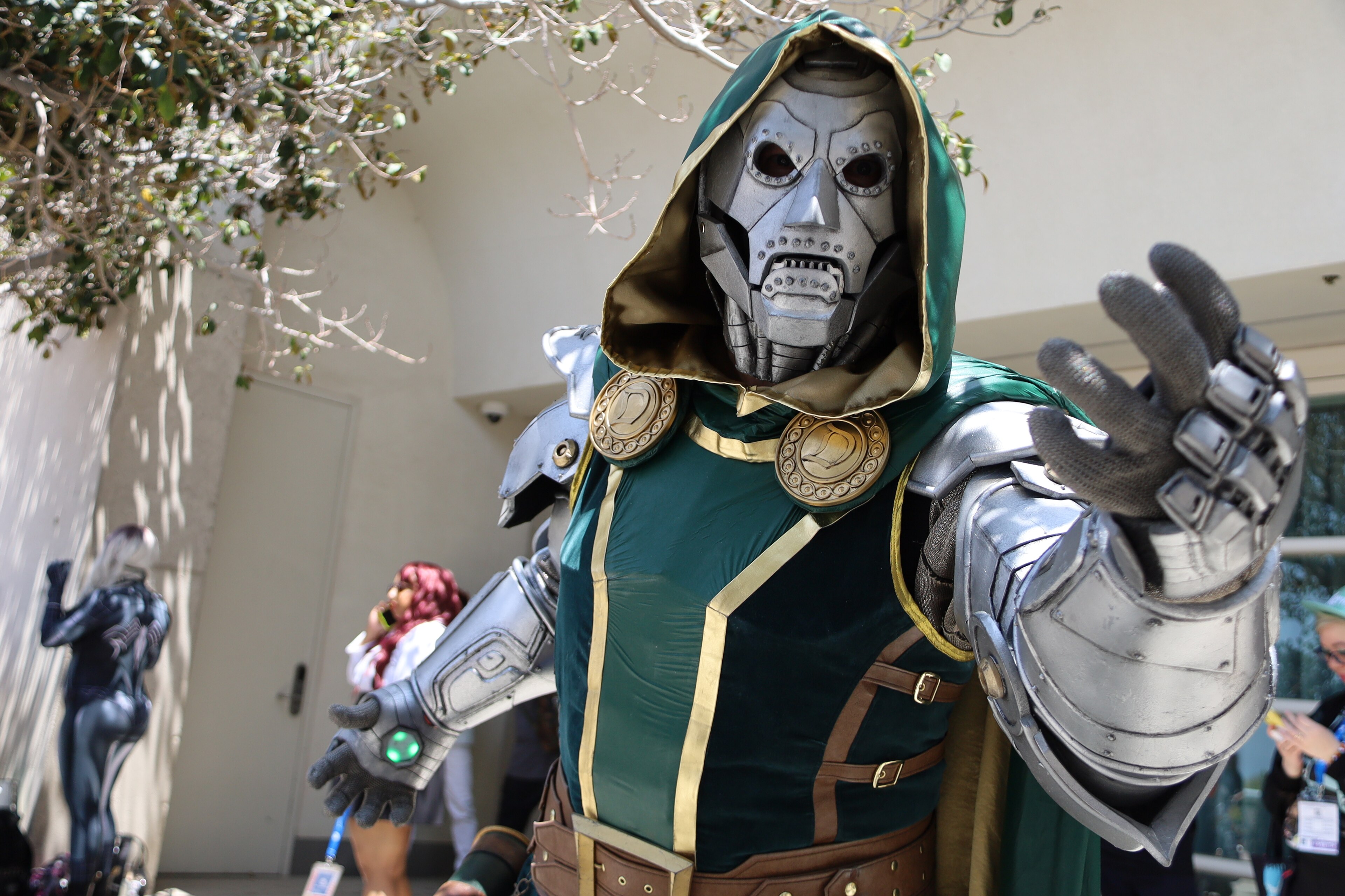 A Doctor Doom cosplayer in a green hood and metal armor reaches toward the camera.