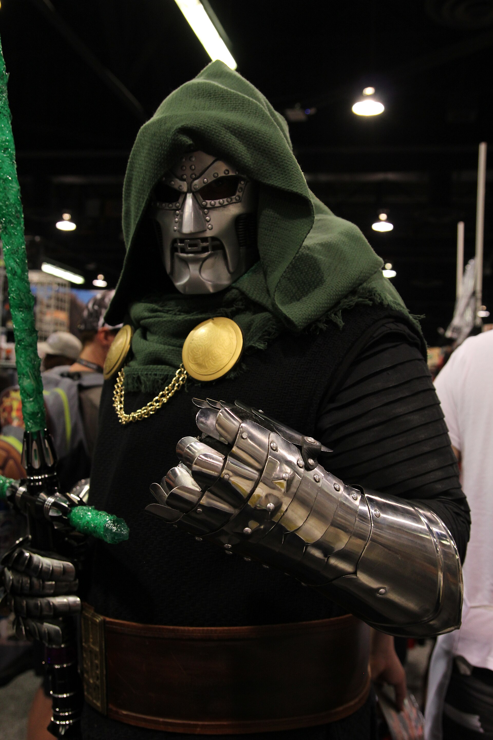A close view of a Doctor Doom cosplayer wearing articulated metal gauntlets and a green hood.