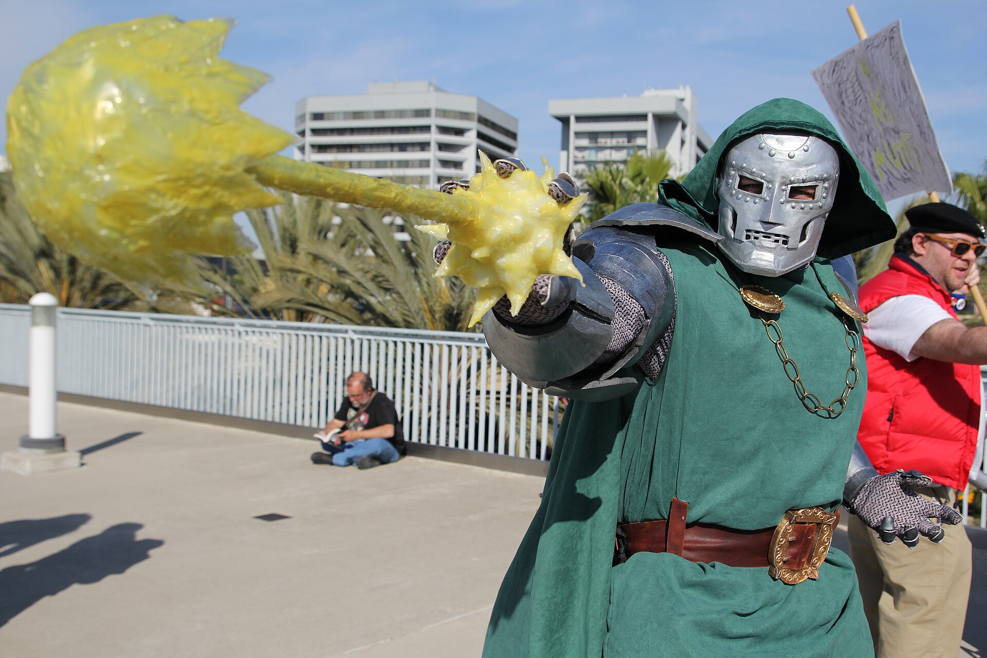 A Doctor Doom cosplayer extends an armored hand with a yellow magical effect from the gauntlet.