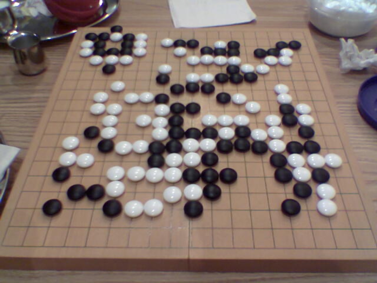 A Go board partway through a game, black and white stones spread across the grid, a cup of tea at the edge of the table