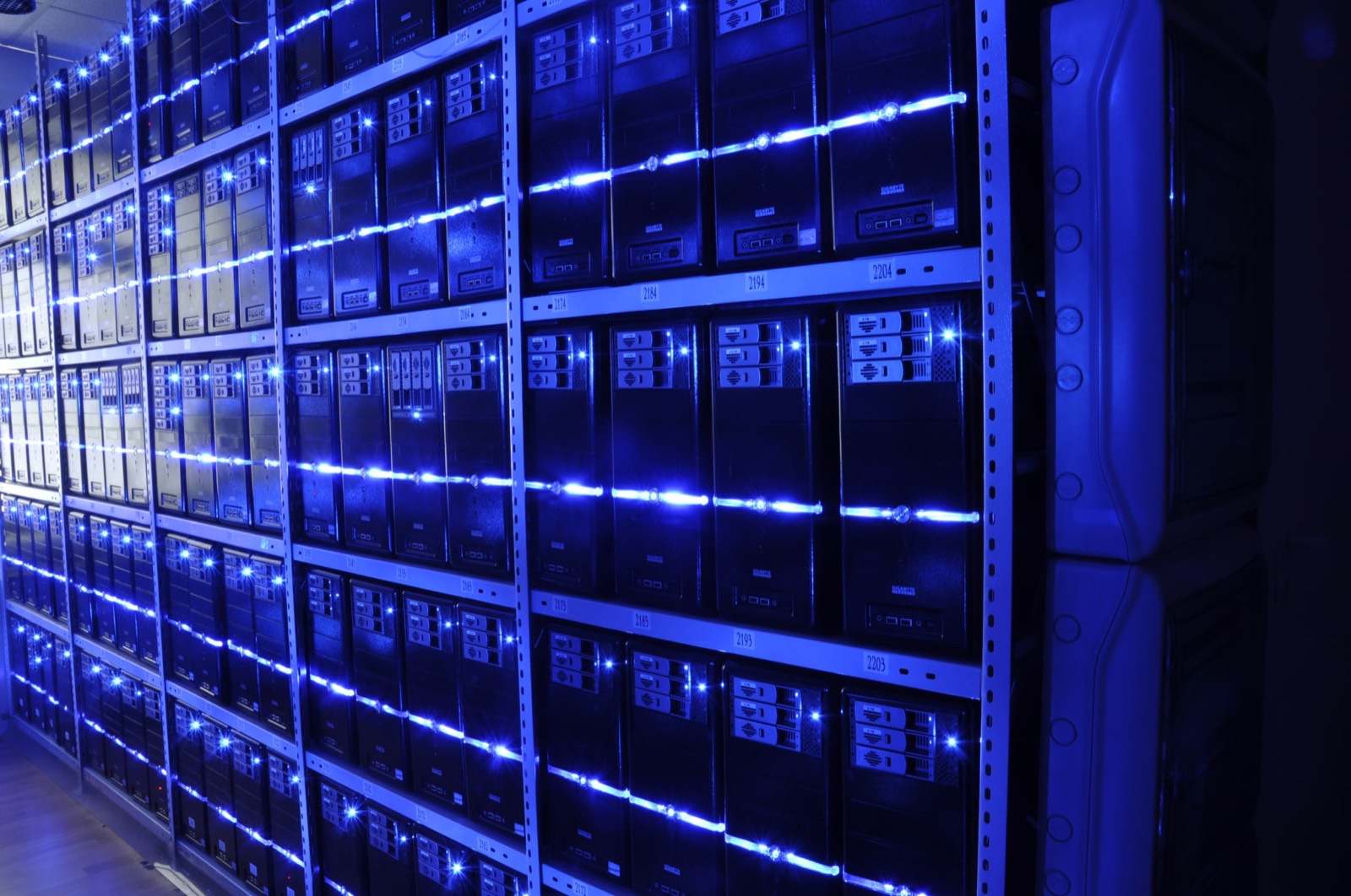 Aisles of server racks receding into the distance inside a data center, lit by cold blue light.