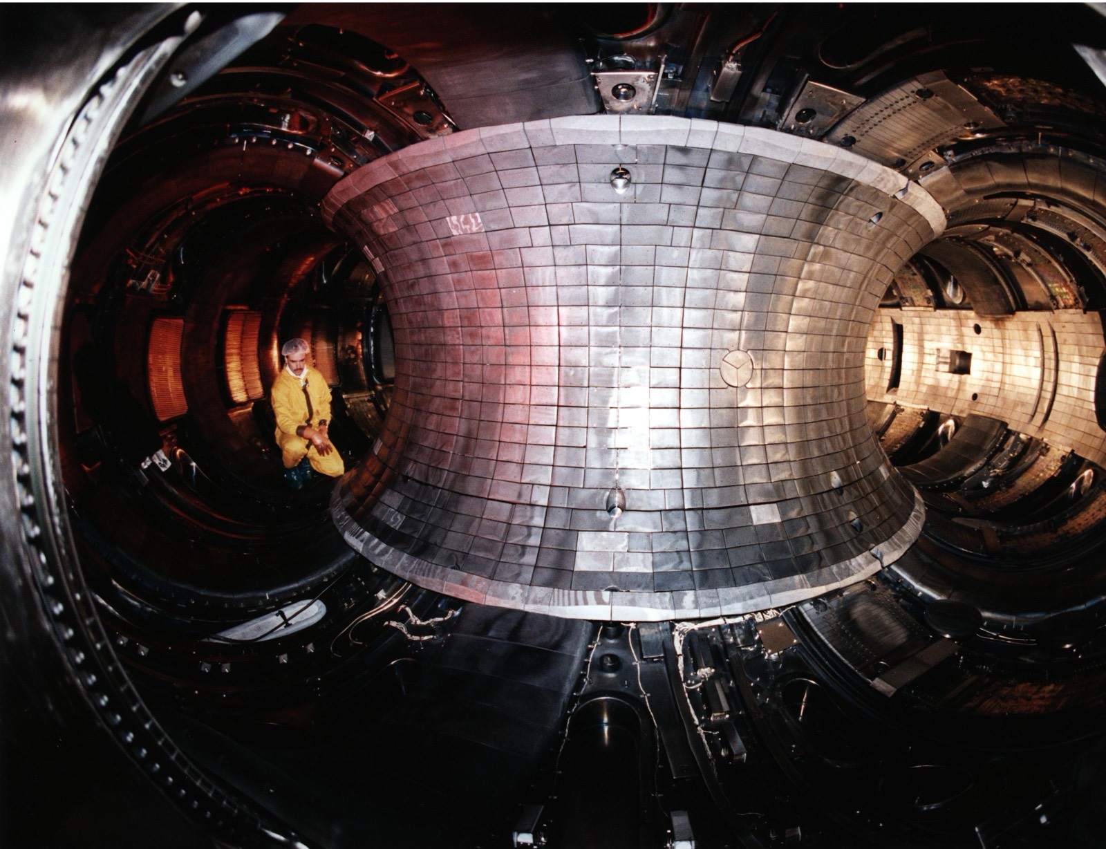 The metallic interior of a tokamak fusion reactor, a curved chamber of intricate machinery.