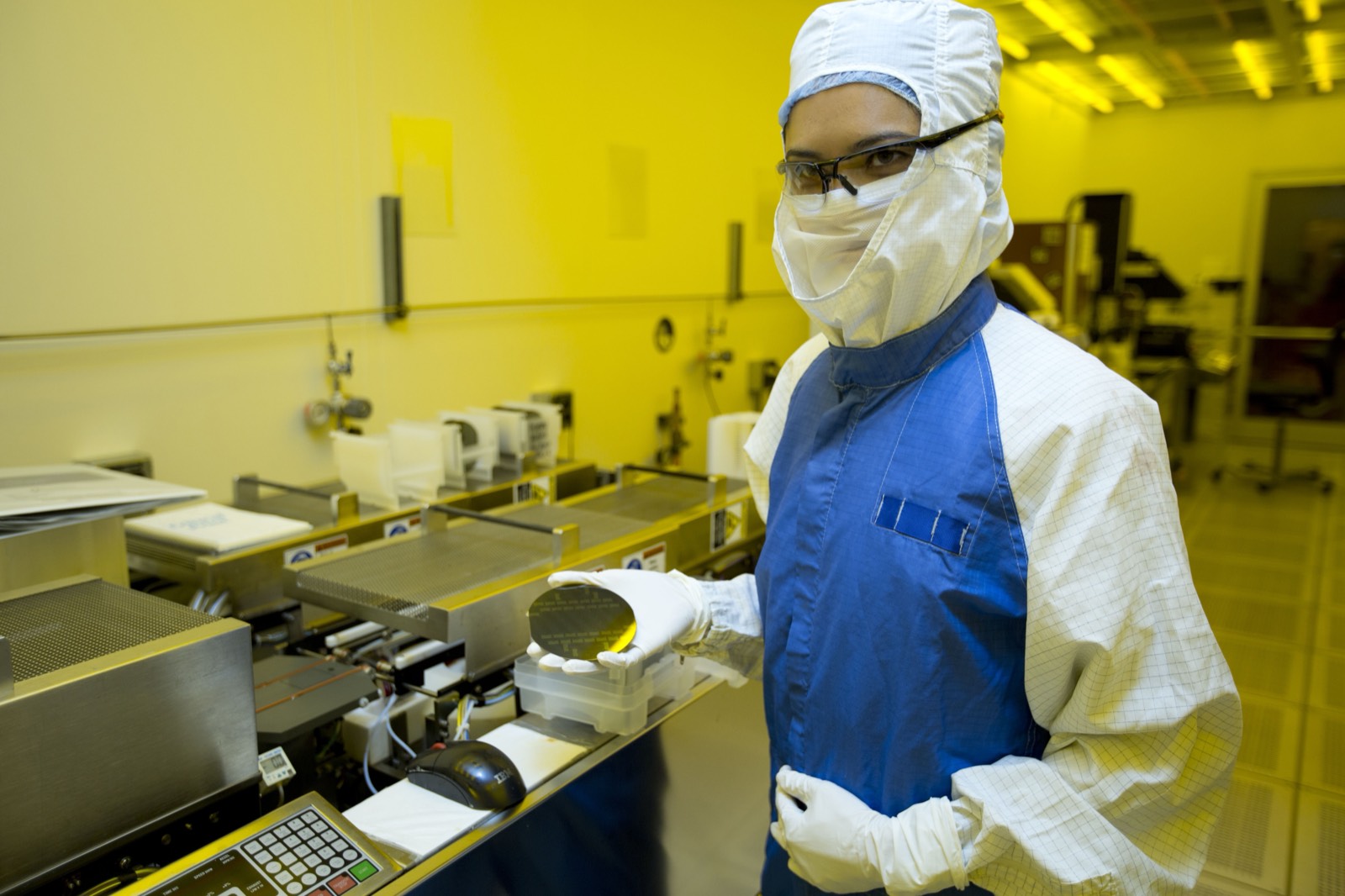A silicon wafer held to the light, its surface shimmering with iridescent color from the etched circuitry.