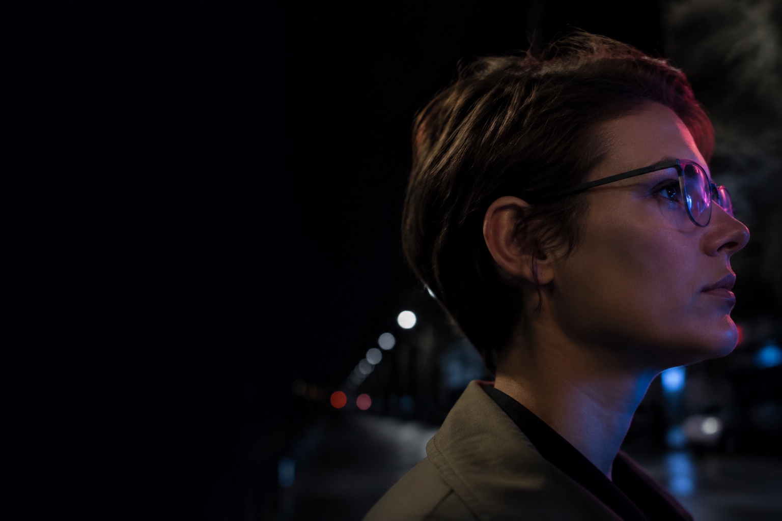 An imagined side profile of a person wearing subtle generic smart glasses in a city at night